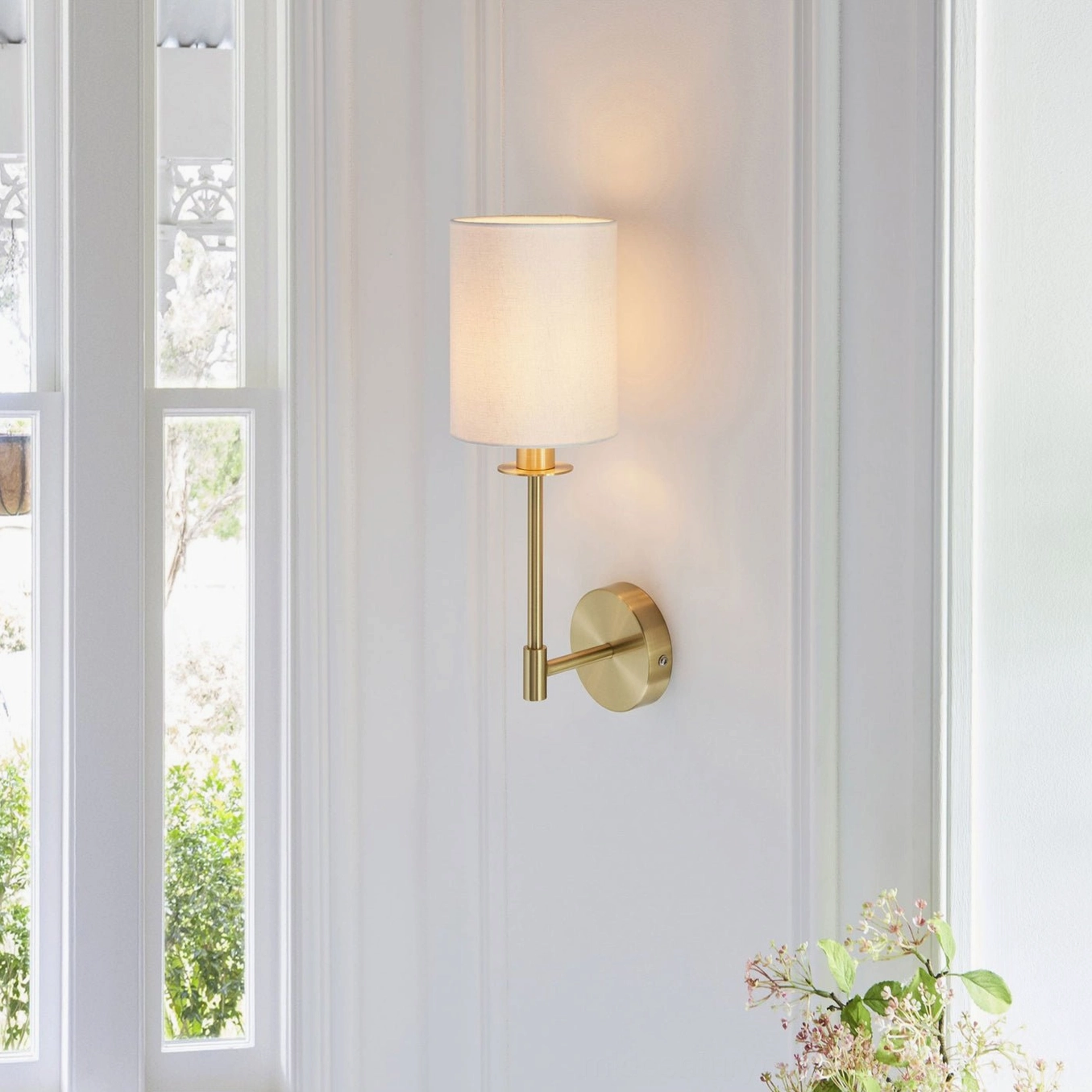 Kington brass wall sconce positioned in modern home corner with floral decor and natural window light