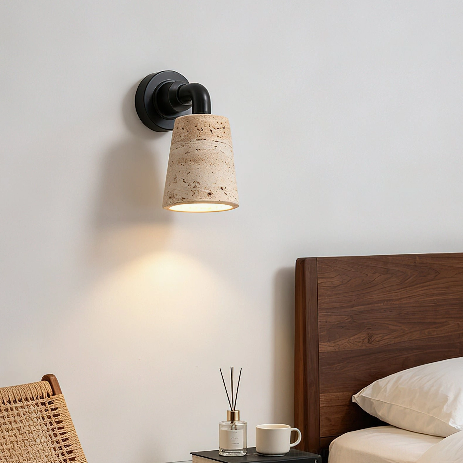 Kiran travertine wall sconce mounted at bedside creating soft downlight illumination in cozy bedroom nook