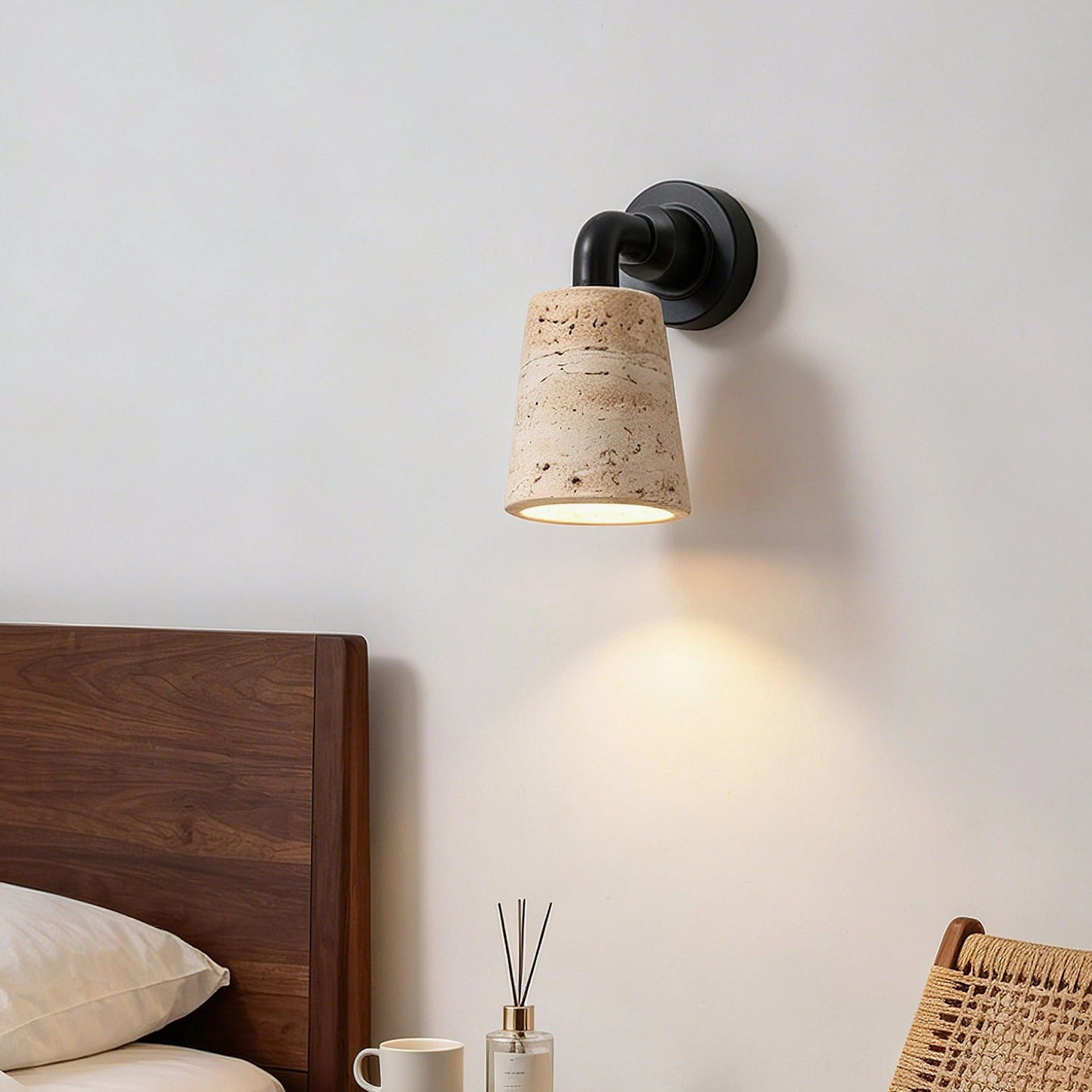 Kiran cylindrical travertine wall light glowing warm in minimalist bedroom with wooden bed frame