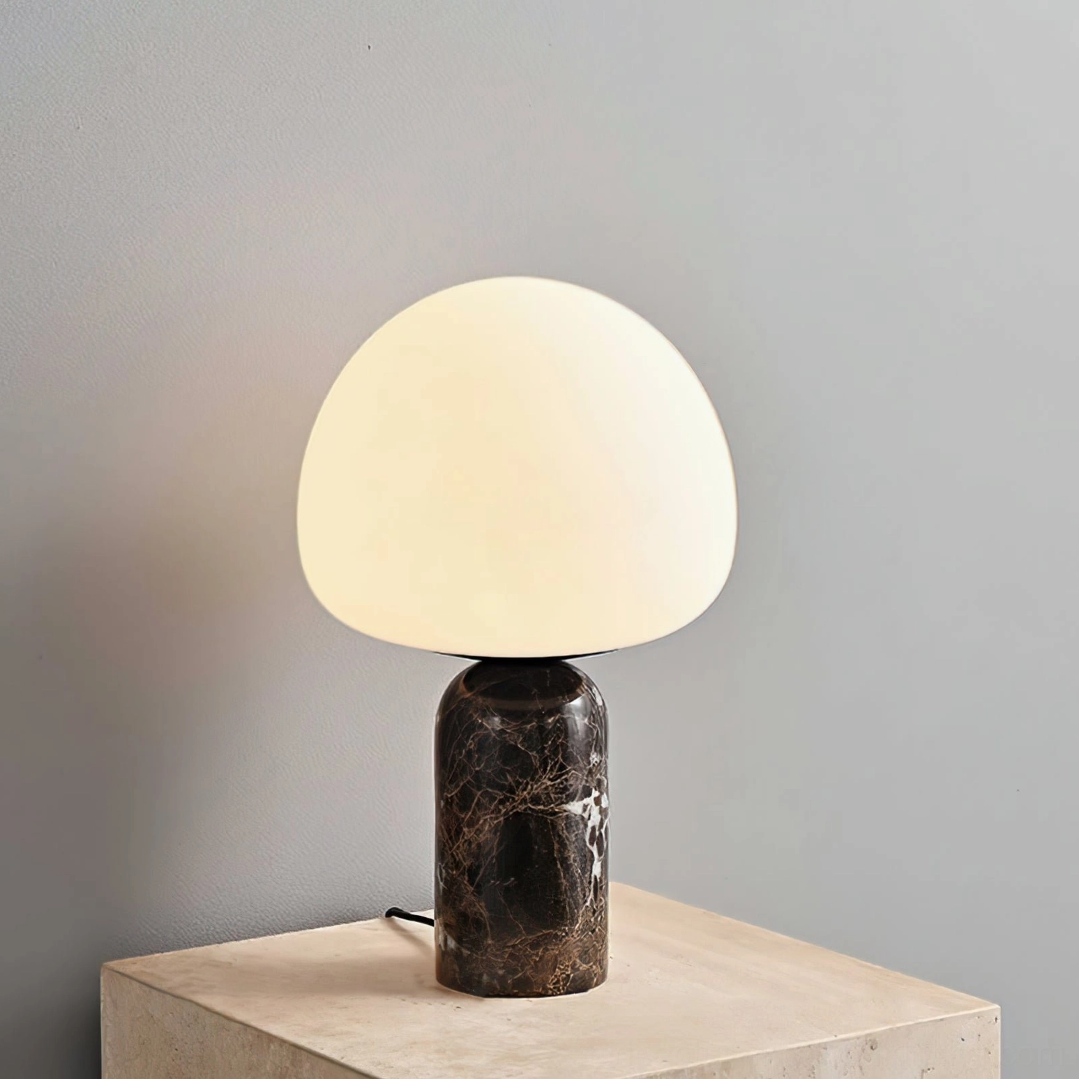 Lit Kizu table lamp emitting warm ambient light, three-quarter view on light stone table