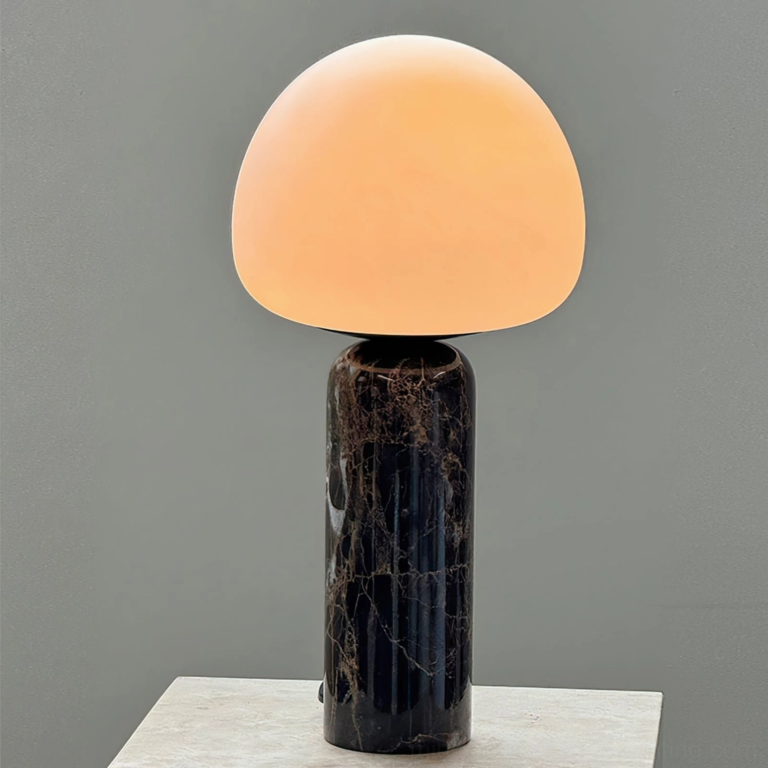 Lit Kizu marble lamp with warm amber glow on light stone side table, three-quarter angle