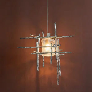 Modern branch pendant lamp with polished silver frame and warm amber glass shade illuminated against dark reddish-brown wall, creating artistic shadow patterns