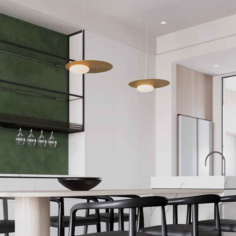 Two brushed gold Kwic disc pendant lamps installed above modern kitchen dining area with green tile backsplash
