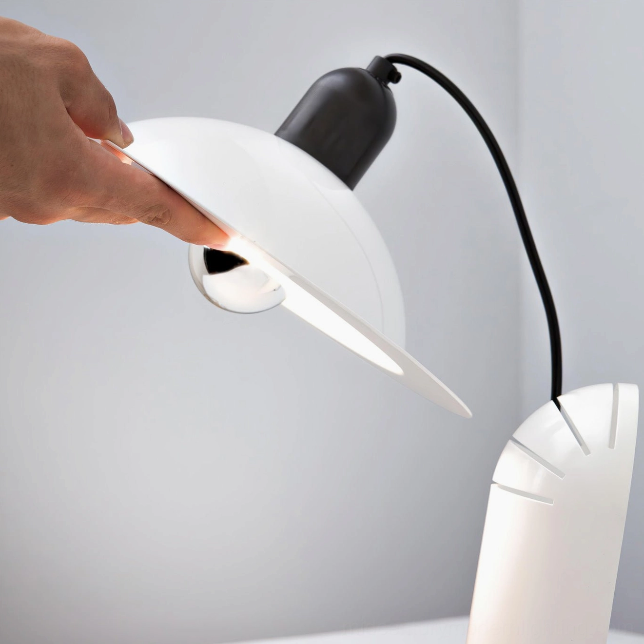 Lampiatta adjustable table lamp with white disc shade and hand demonstrating directional light adjustment capability