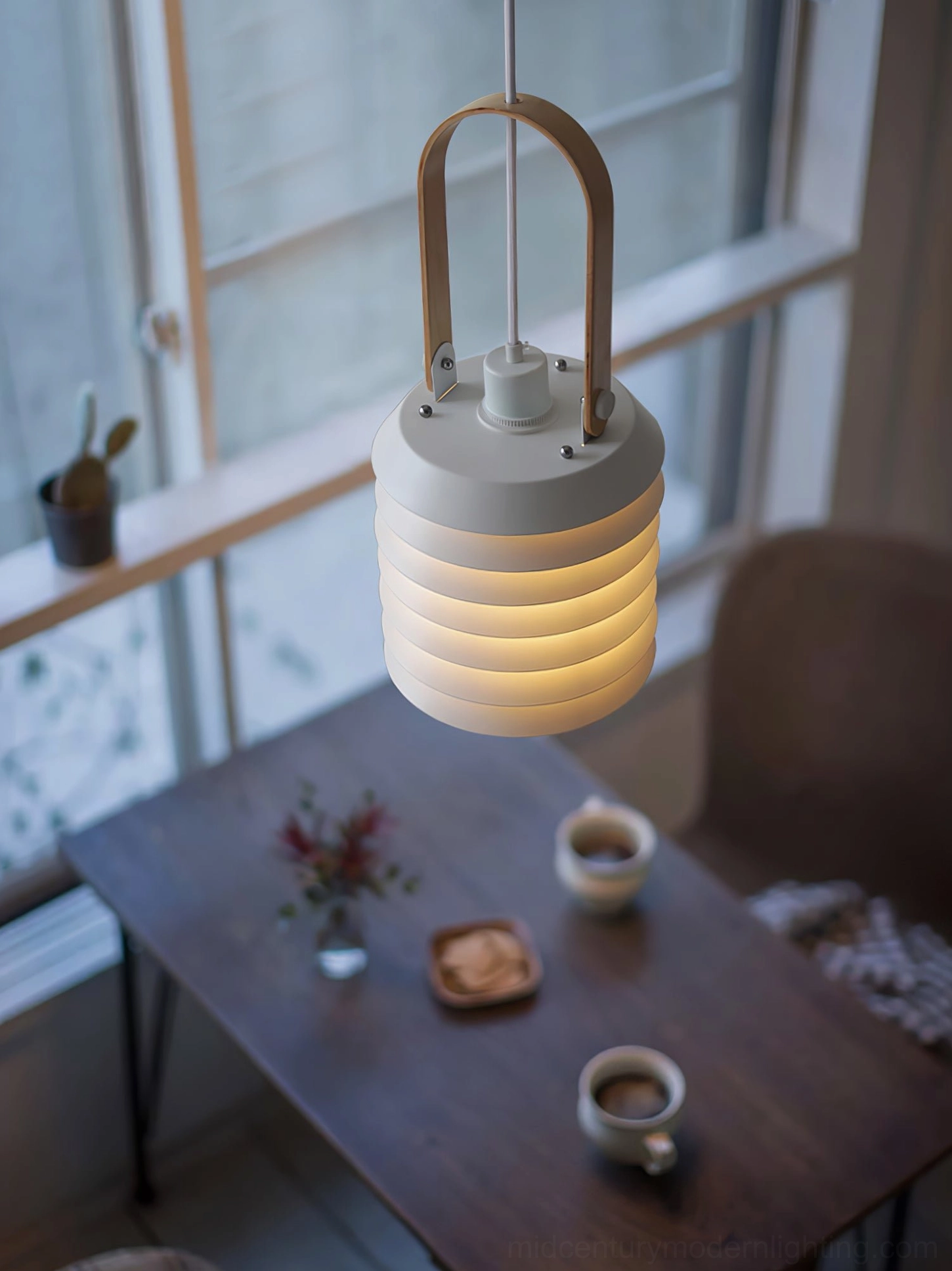 Single tiered pendant lamp with wooden hanging strap beside dining table with warm table setting