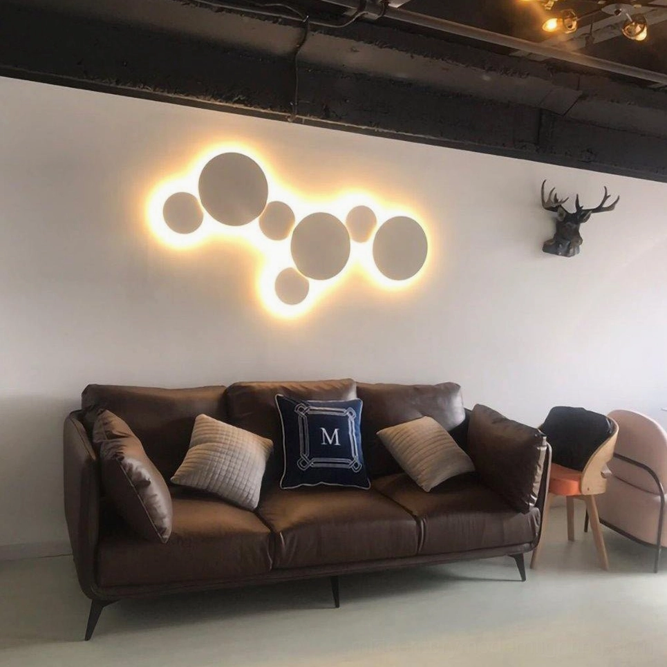 Large backlit mixed-size geometric disc wall lamp in cozy modern living room with sofa creating warm sculptural light art