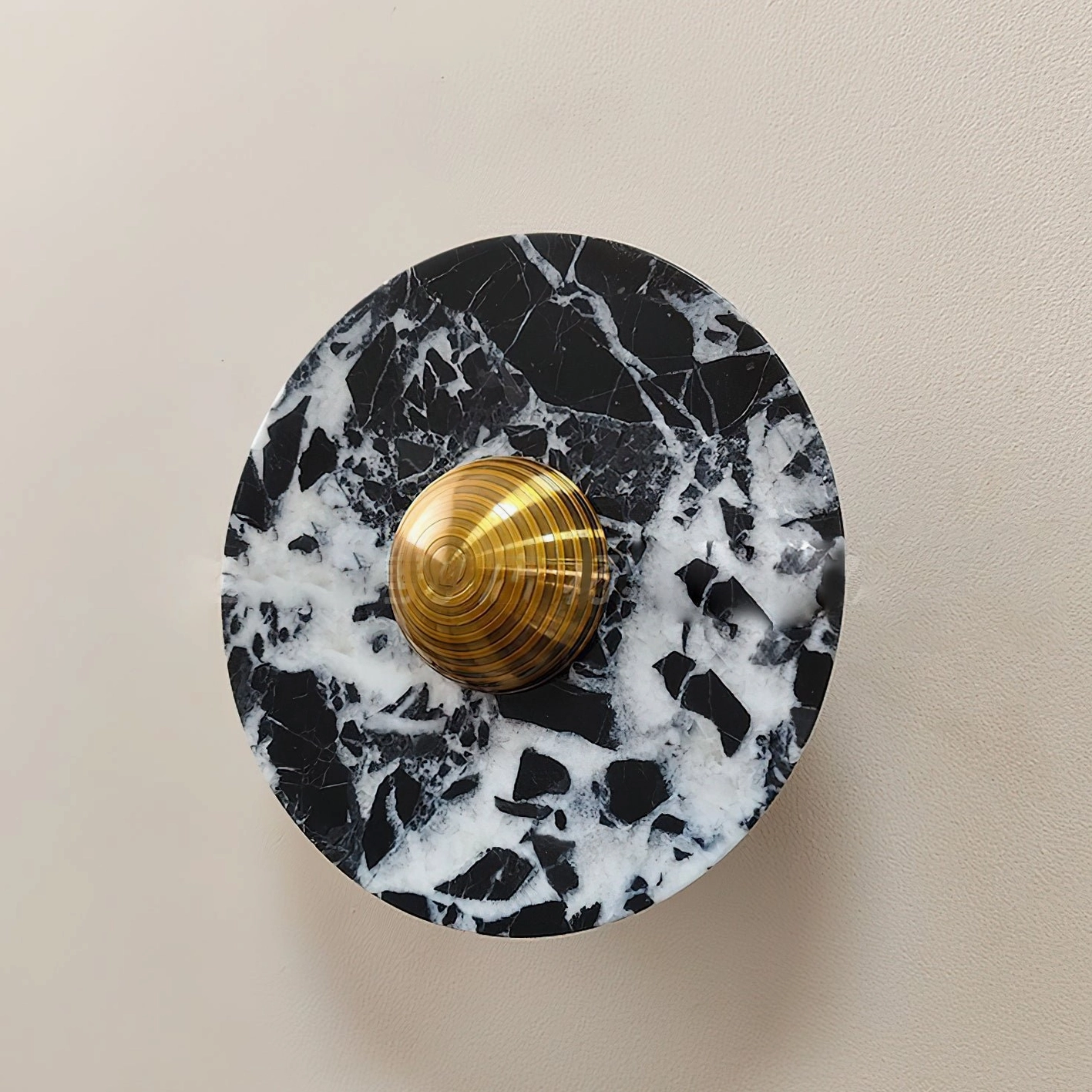 Large format black and white marble geometric wall lamp with brass accent fixture mounted on beige wall