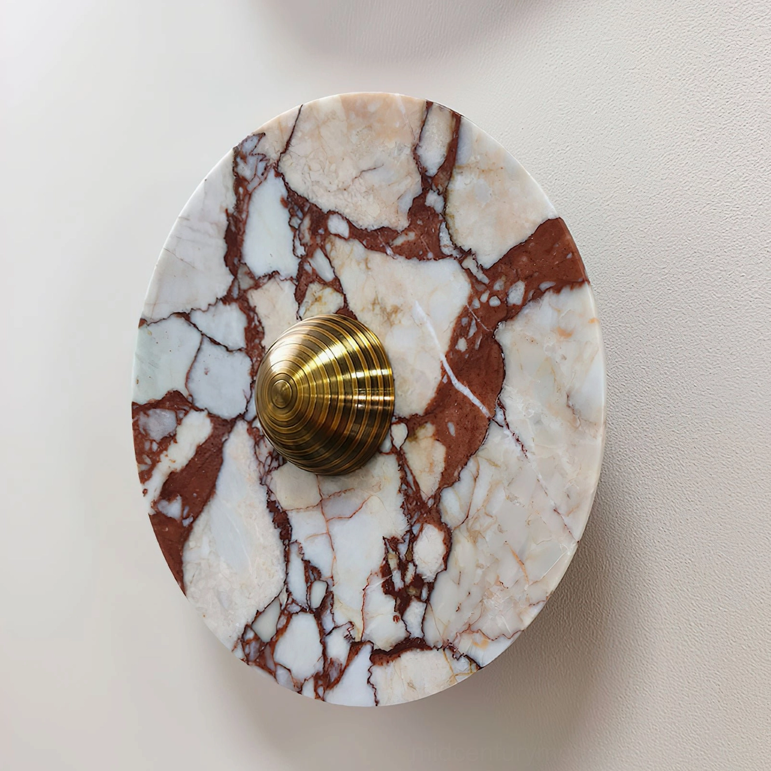Large diameter red and white marble wall lamp with brass fixture accent mounted on interior wall