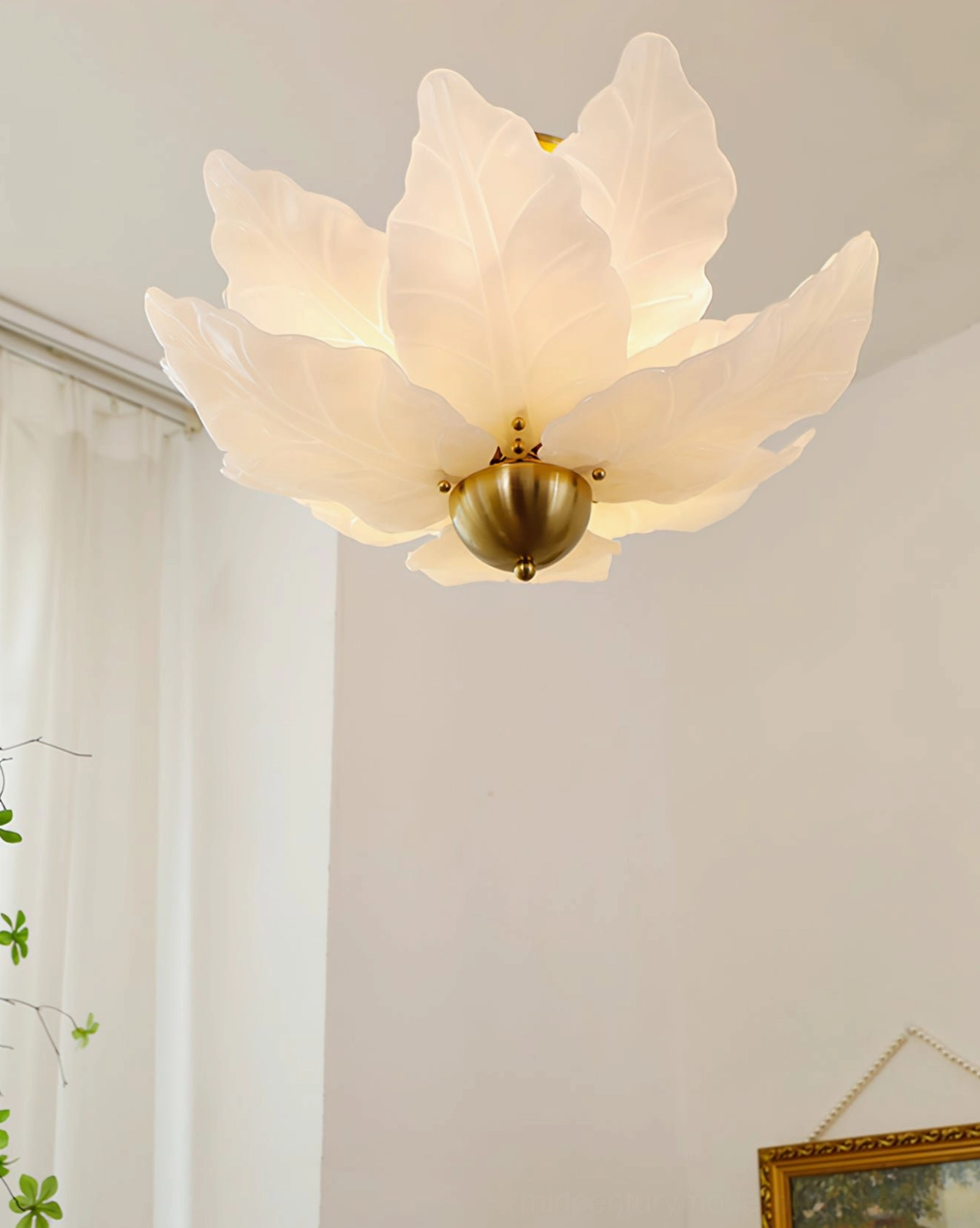 Warm cottage-core leaf ceiling lamp close-up with creamy yellow-toned glass and brass hardware on white wall with sheer curtain