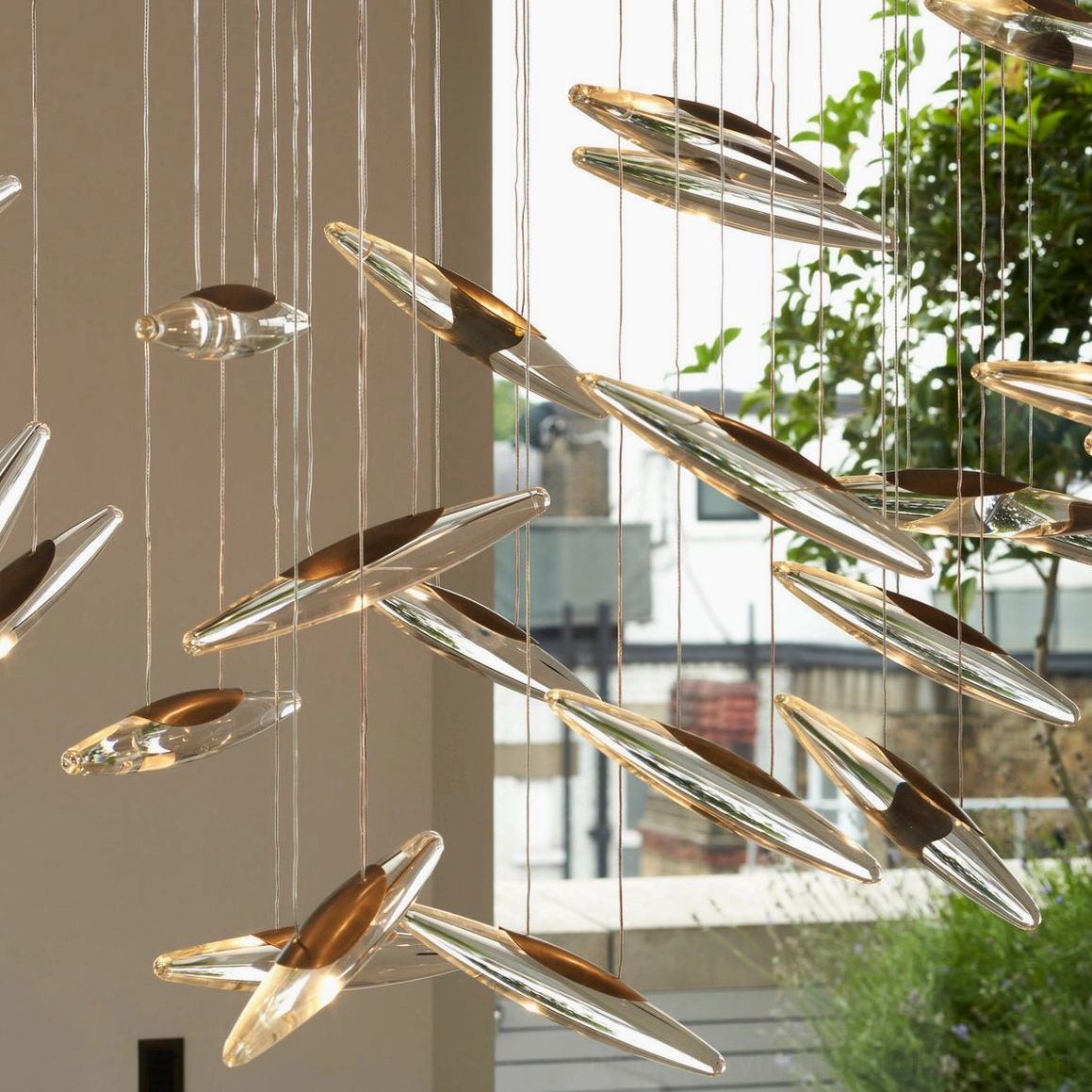 Leaf-shaped glass pendant chandelier close-up showing polished metallic and clear glass elements with greenery background