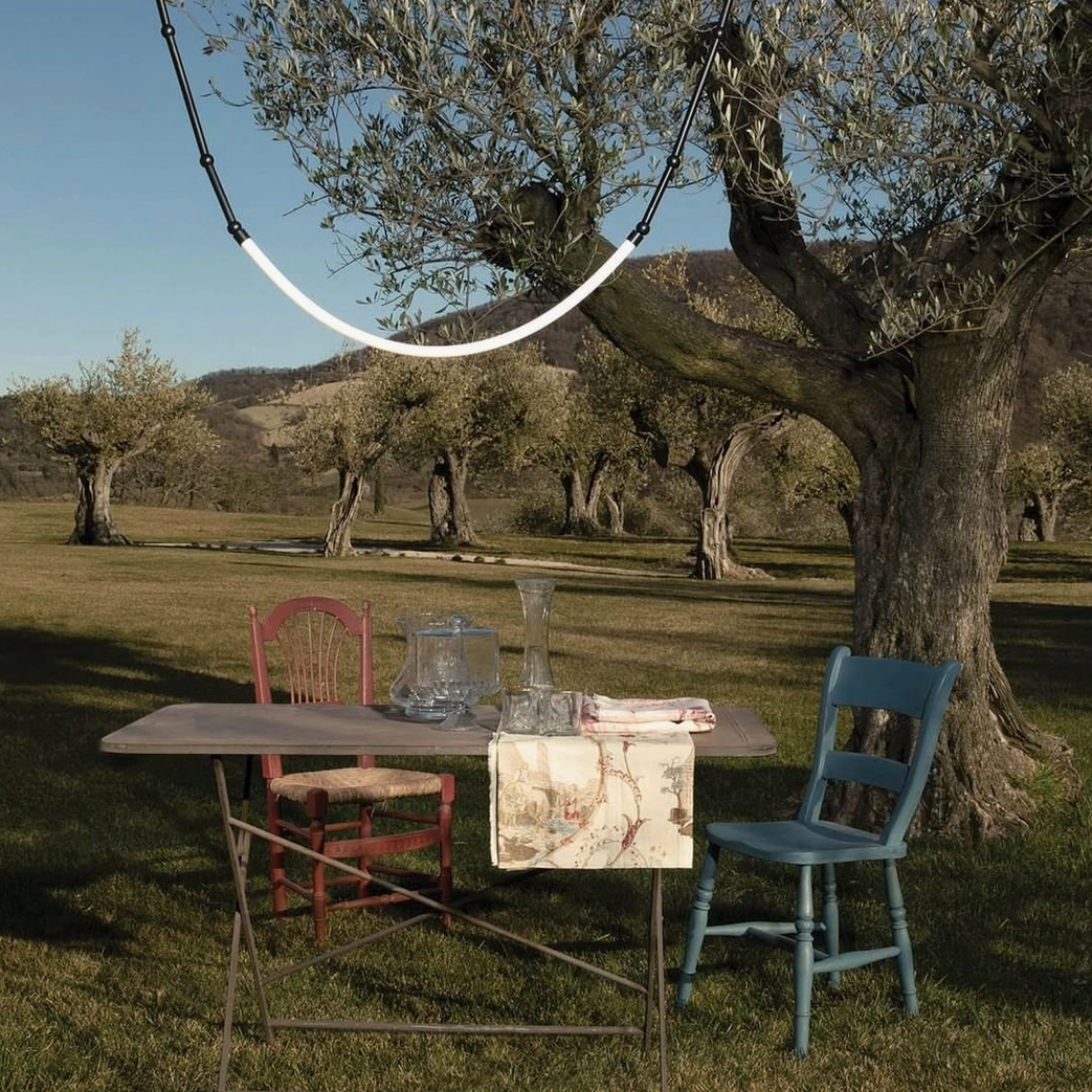 Outdoor curved pendant light fixture suspended above olive orchard dining area, warm minimalist ambiance