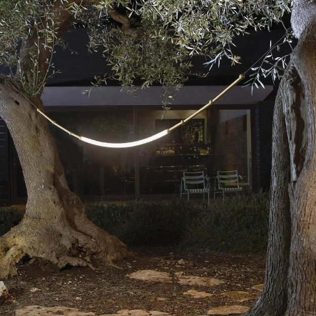 Single curved Leda LED pendant lamp accent lighting over olive tree backyard patio, warm minimalist ambiance