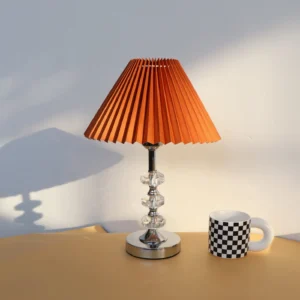 Mid-century modern Lenny table lamp in orange with pleated shade on minimalist desktop with ceramic mug