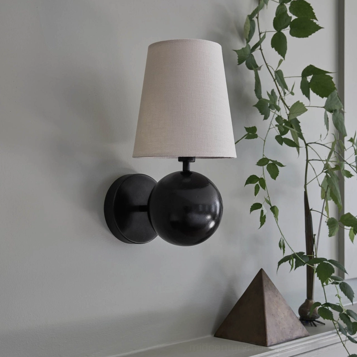 Leoda wall sconce mounted in bedroom corner beside green potted plant, neutral farmhouse interior styling