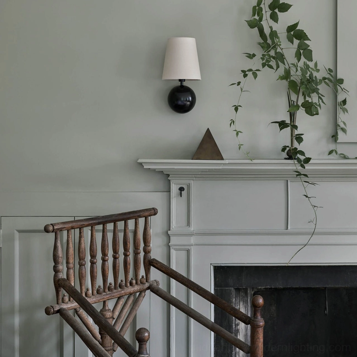 Leoda wall sconce with white fabric shade and black spherical brass base mounted beside fireplace foyer