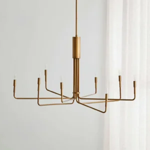 Lepanto brass chandelier angled front view showcasing warm matte brass finish and slim metal arms suspended from ceiling in bright residential dining room with white curtains