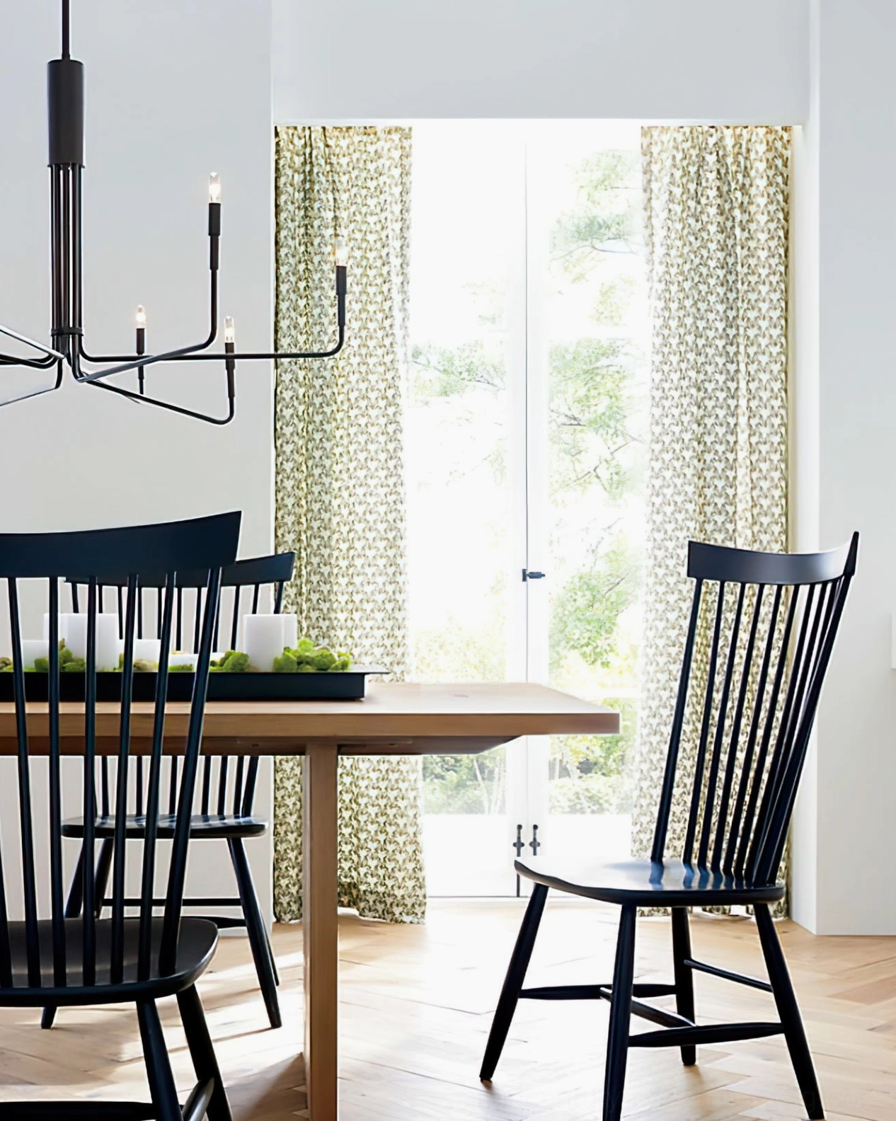 Lepanto compact black 8-head chandelier side view in bright casual dining space showing slim metal design proportions and elegant black finish against white background