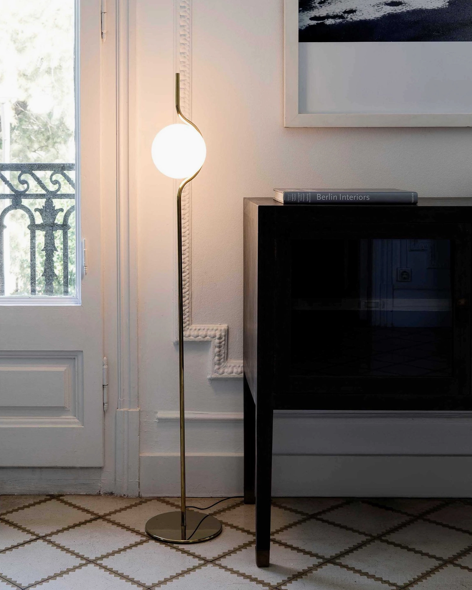 Gold brass Levita floor lamp in bright tiled entryway beside console table and window for ambient lighting