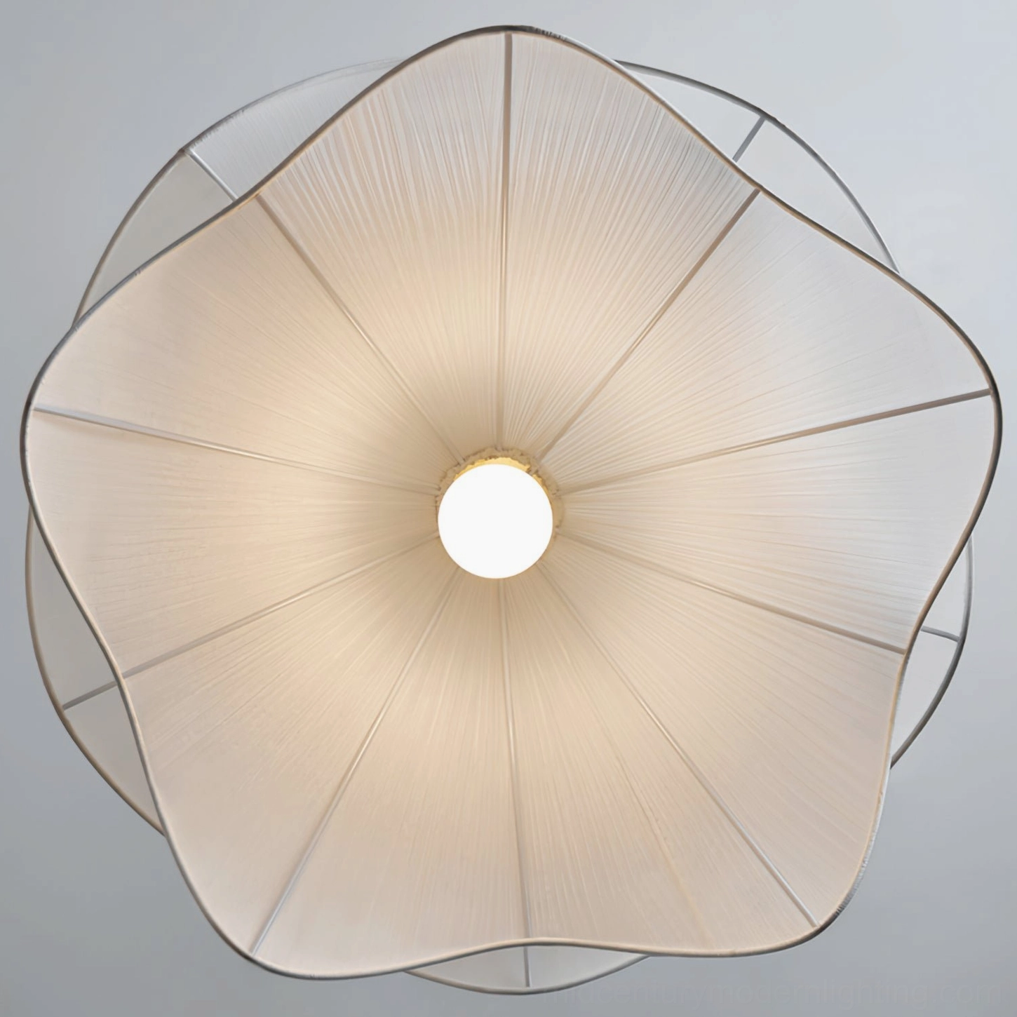 Illuminated bottom view of Lia pendant lamp showing radial flower-like pleated design when lit, warm luminescence and spherical geometry