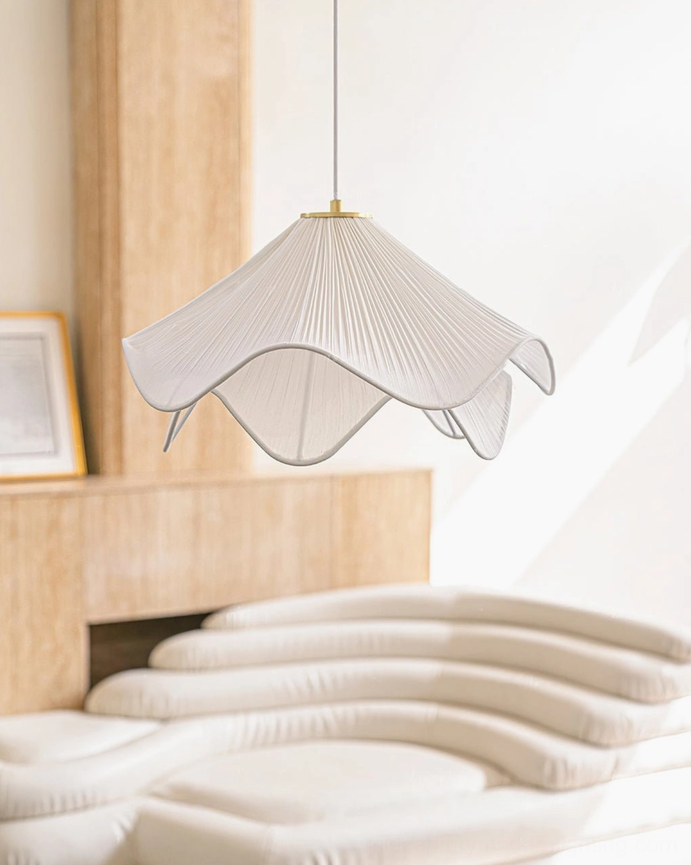 Lia mid-century modern pendant lamp with pleated fabric shade, hanging in bedroom setting with wooden bed frame and fireplace, soft off-white color