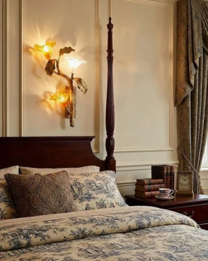 Hand-cast brass lily branch sconce mounted in traditional four-poster bedroom interior with warm ambient lighting