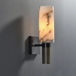 Modern alabaster marble wall sconce illuminated with warm light, installed on grey indoor wall showing fluted brass base detail