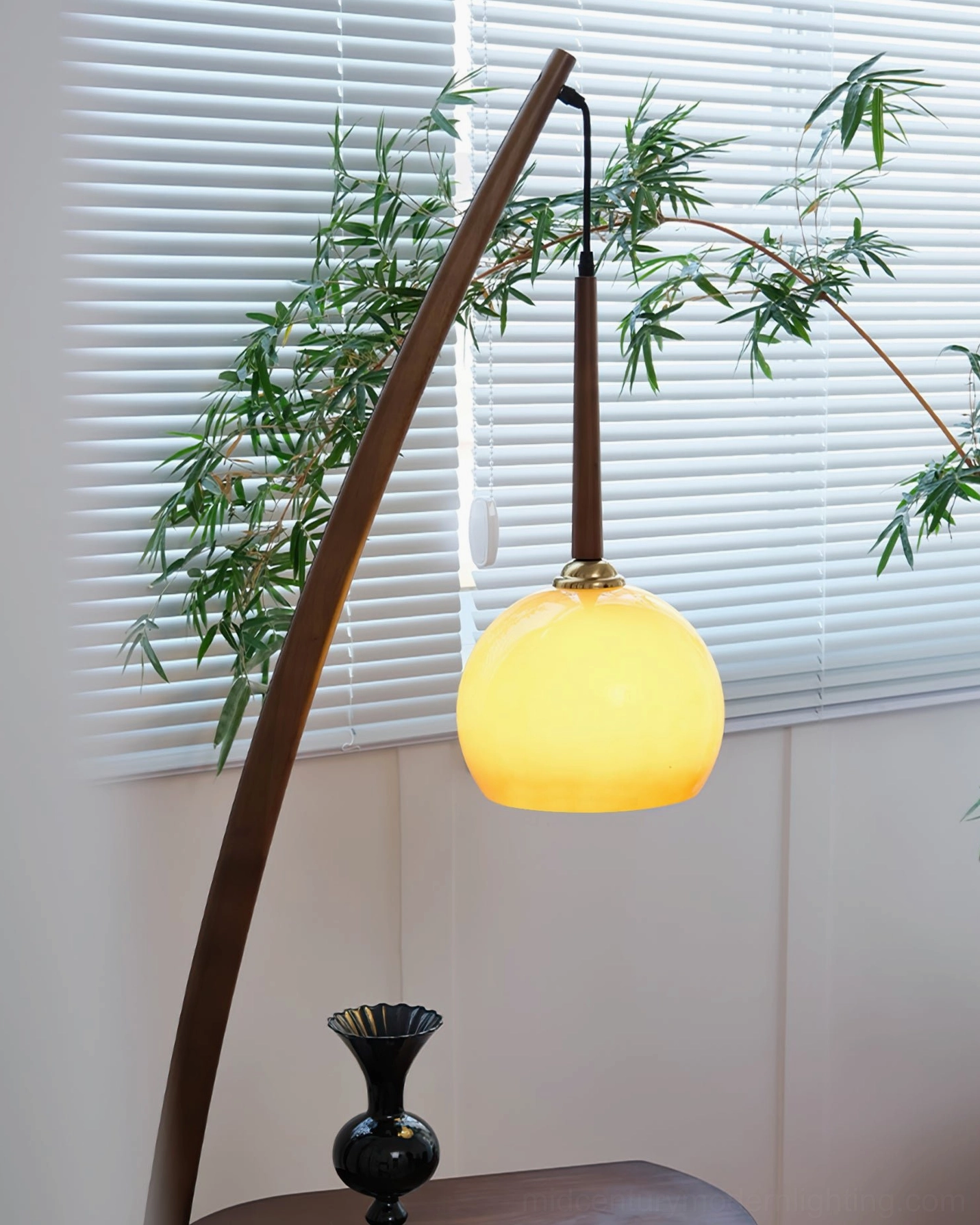 Arc floor lamp with side table lit up, warm yellow amber glass shade, window blinds and plants