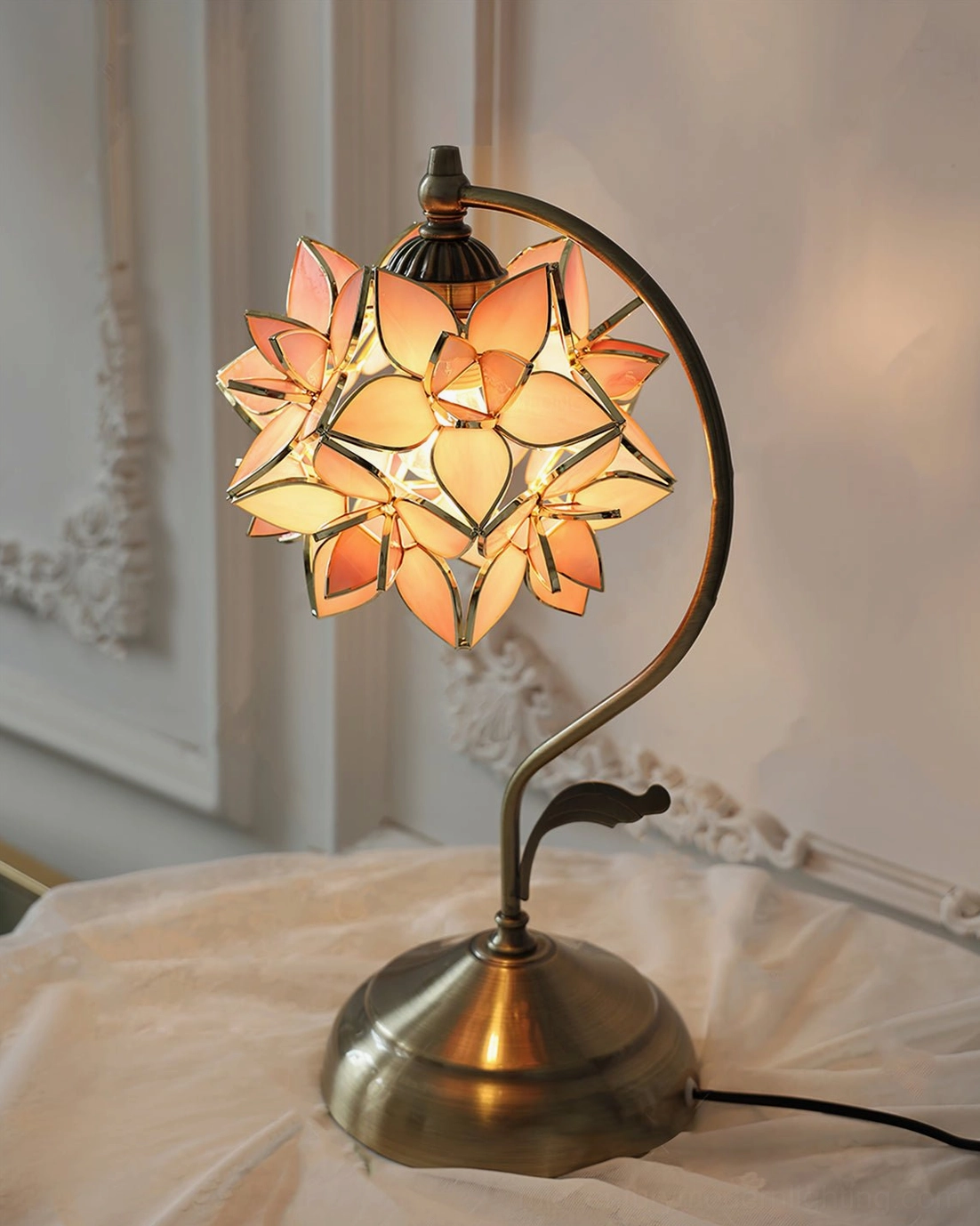 Illuminated capiz flower lamp with stable bronze metal base, glowing stained glass flower petals creating soft ambient light