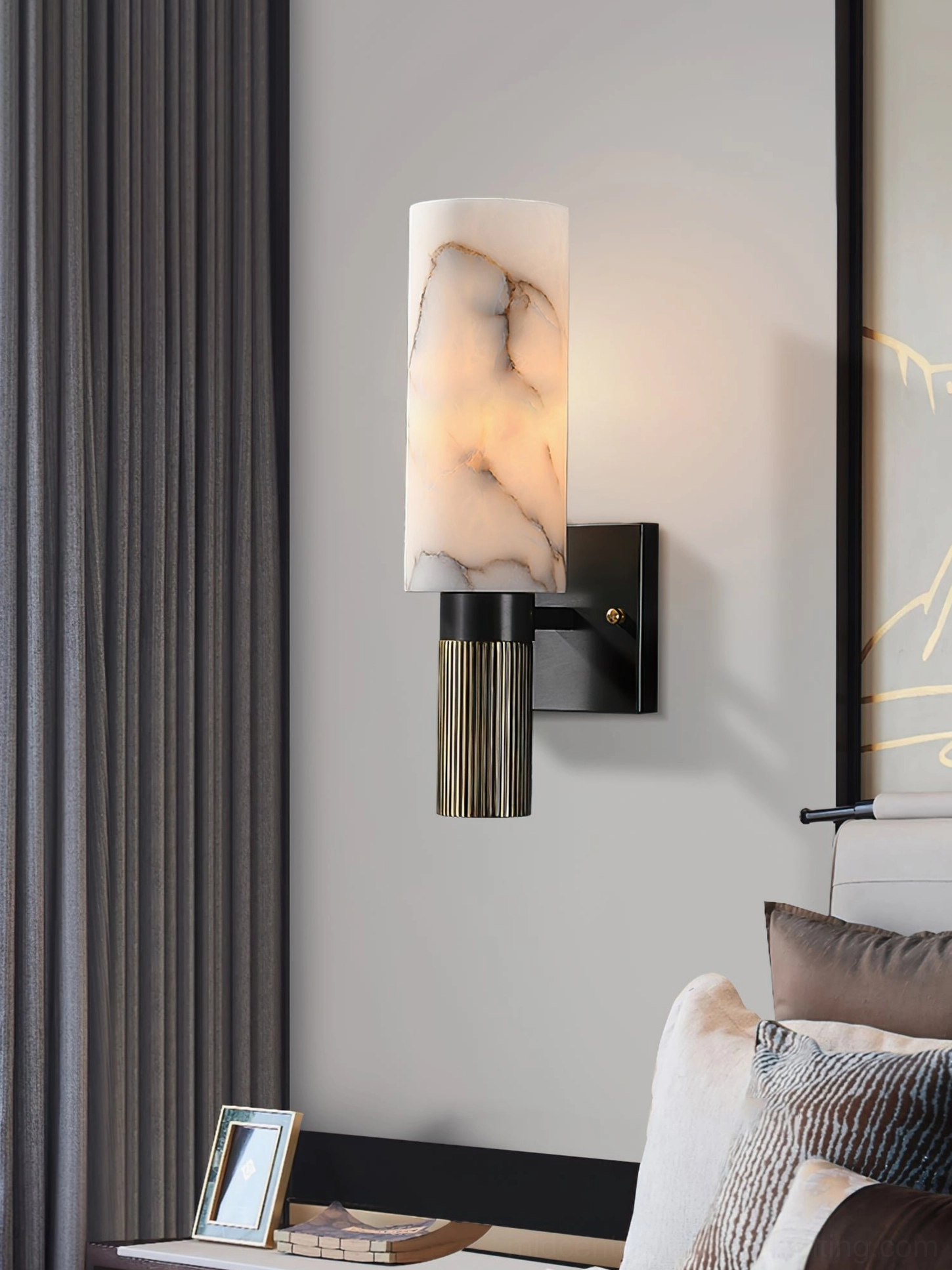 Cylindrical alabaster wall lamp front view with lit warm glow, vertical fluted brass base architectural detail
