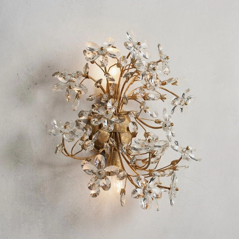 Illuminated gold crystal flower wall lamp mounted on textured wall, warm LED glow highlighting refracted light through faceted petals