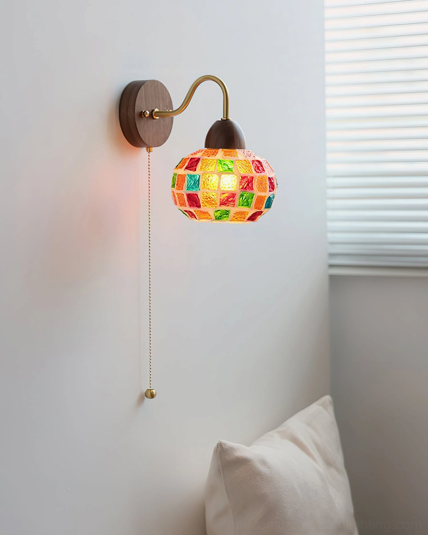 Illuminated mosaic wall lamp casting jewel-toned light in bedroom with throw pillows - side angle view