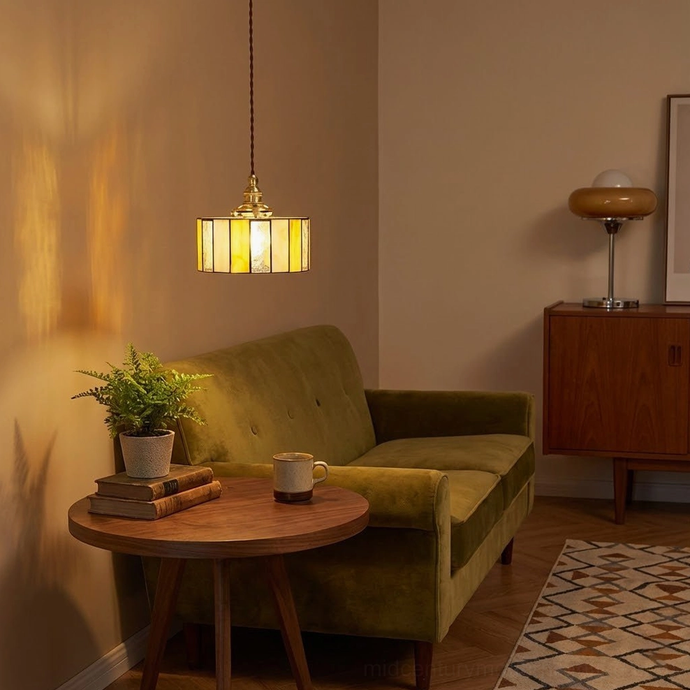 Tiffany-style stained glass pendant lamp above living room with olive green velvet sofa, glowing warm amber glass shade