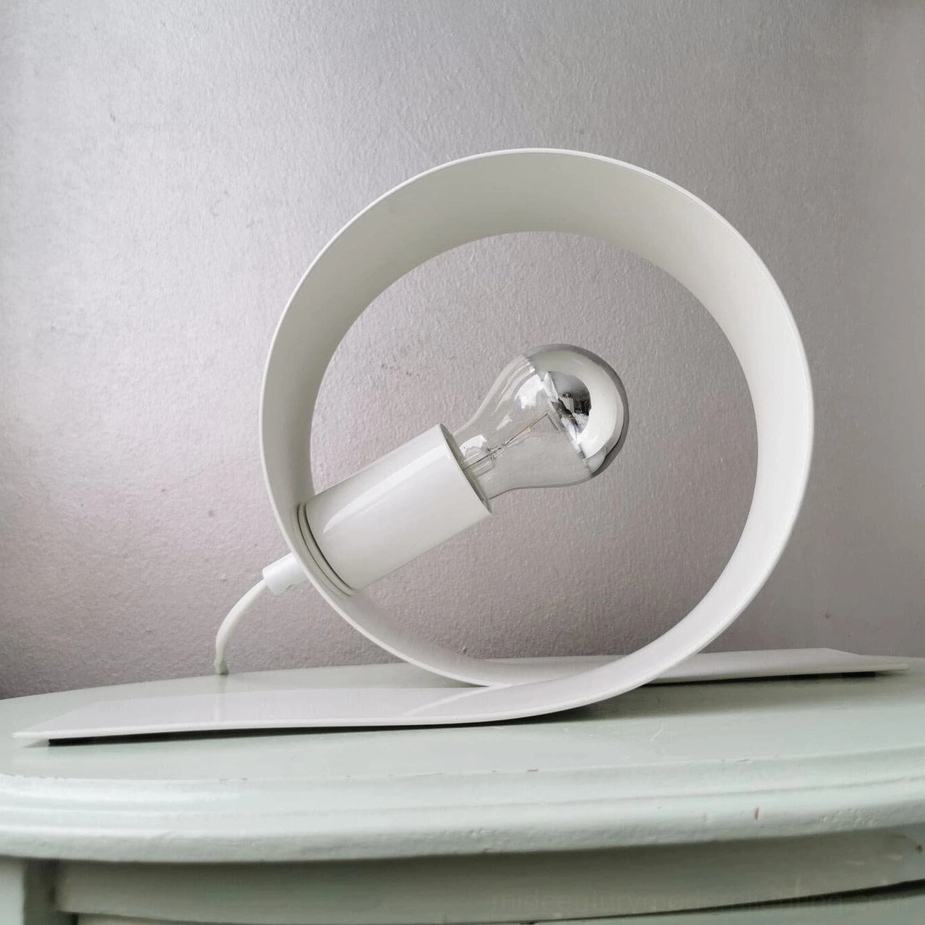Circular looping table lamp in bedroom bedside setting with exposed bulb details