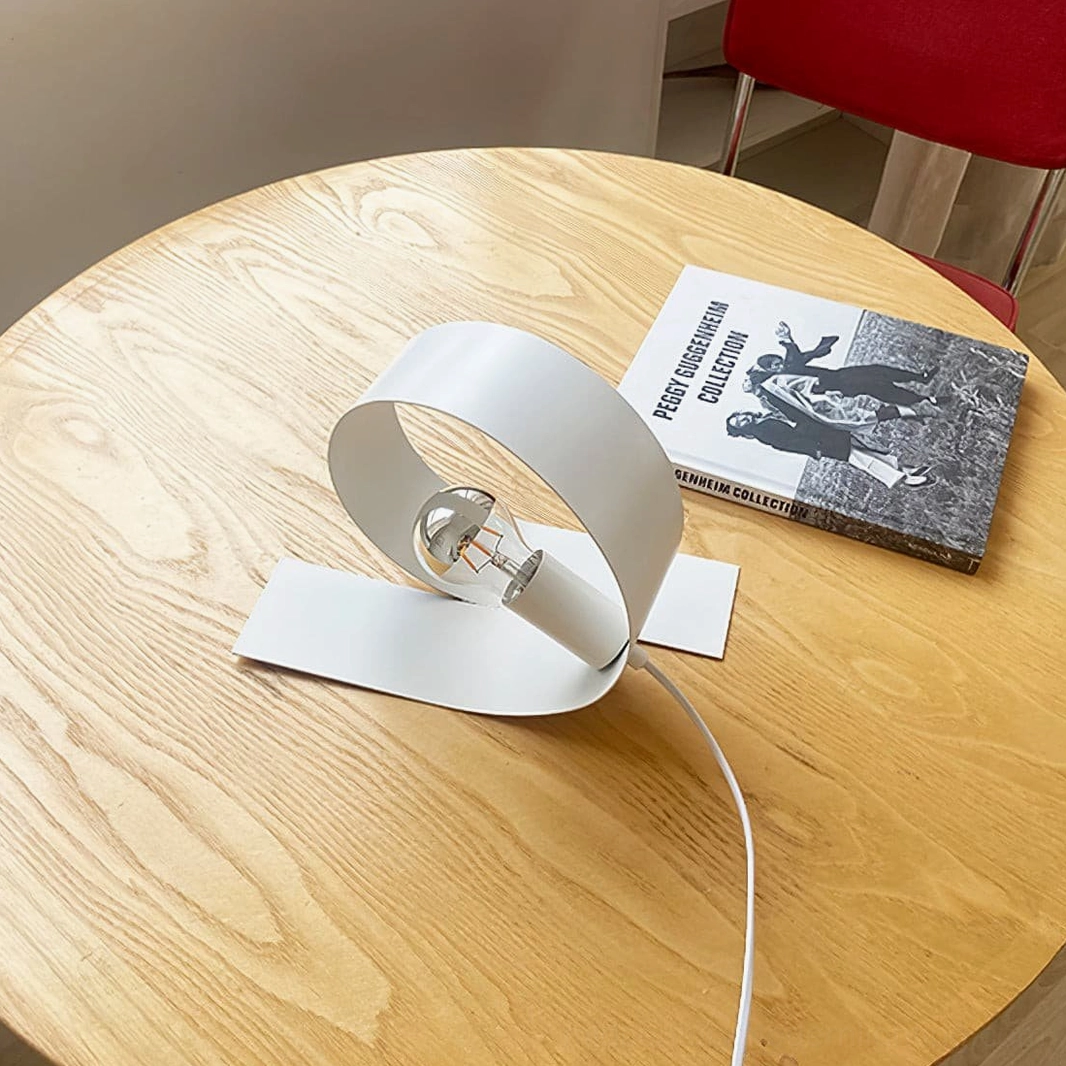 Minimalist looping lamp on dining table paired with art books and red accent chair