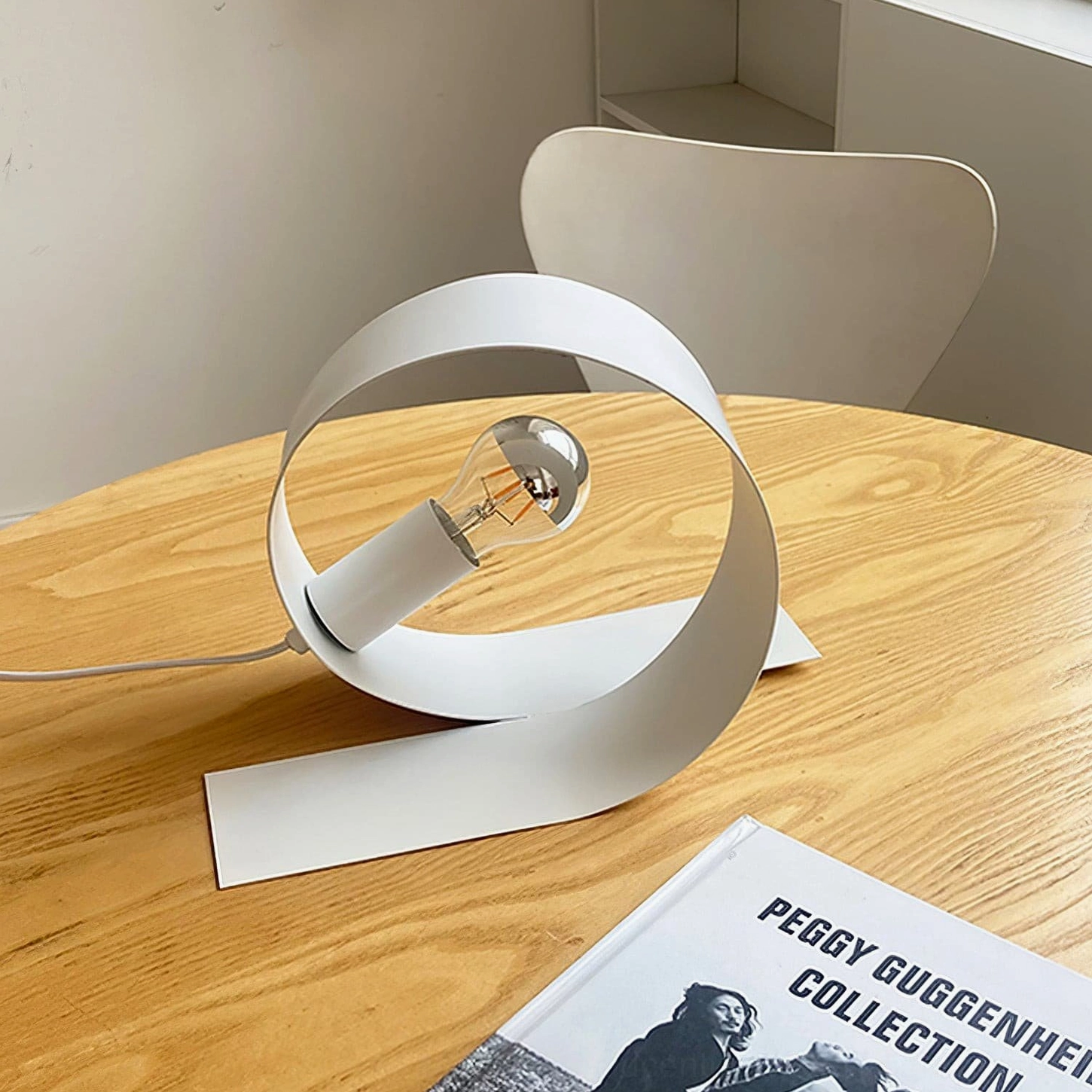 Minimalist looping lamp styled on dining table with wooden round base and art book decor