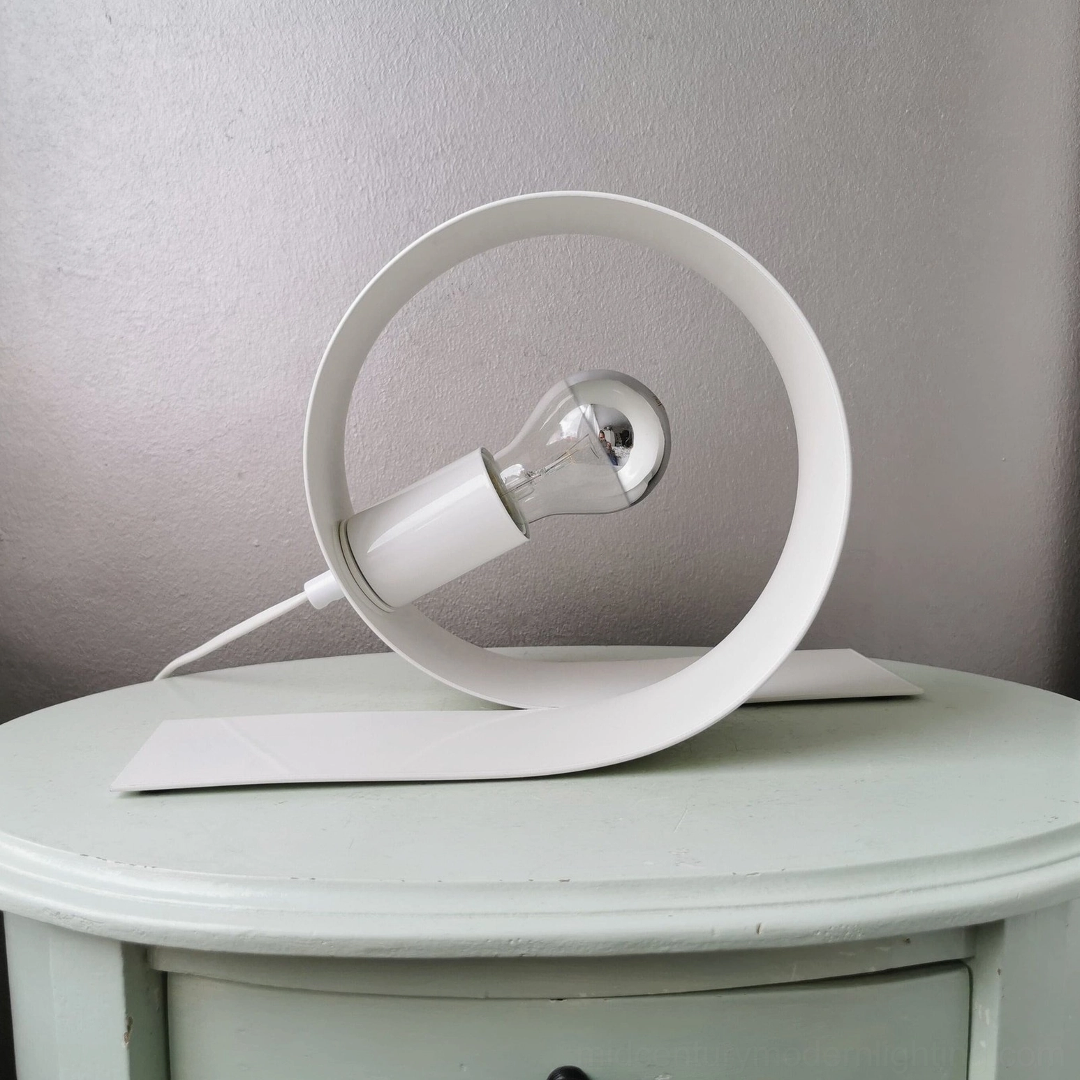White metal looping lamp on bedroom nightstand with minimalist modern aesthetic
