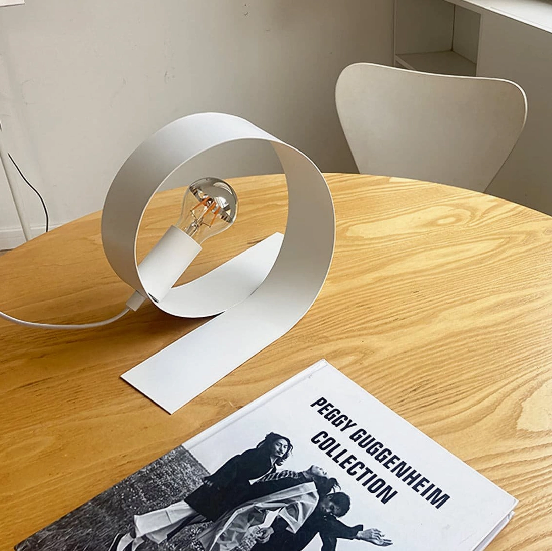 White matte metal looping lamp with curved ribbon body on wooden dining table