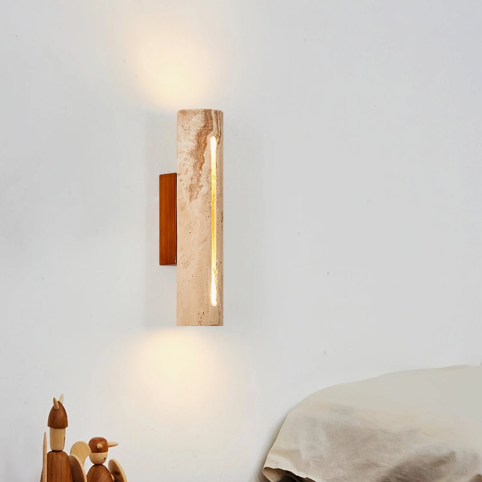 Lorelei travertine wall sconce installed in modern bedroom corner with soft warm lighting and wooden decor
