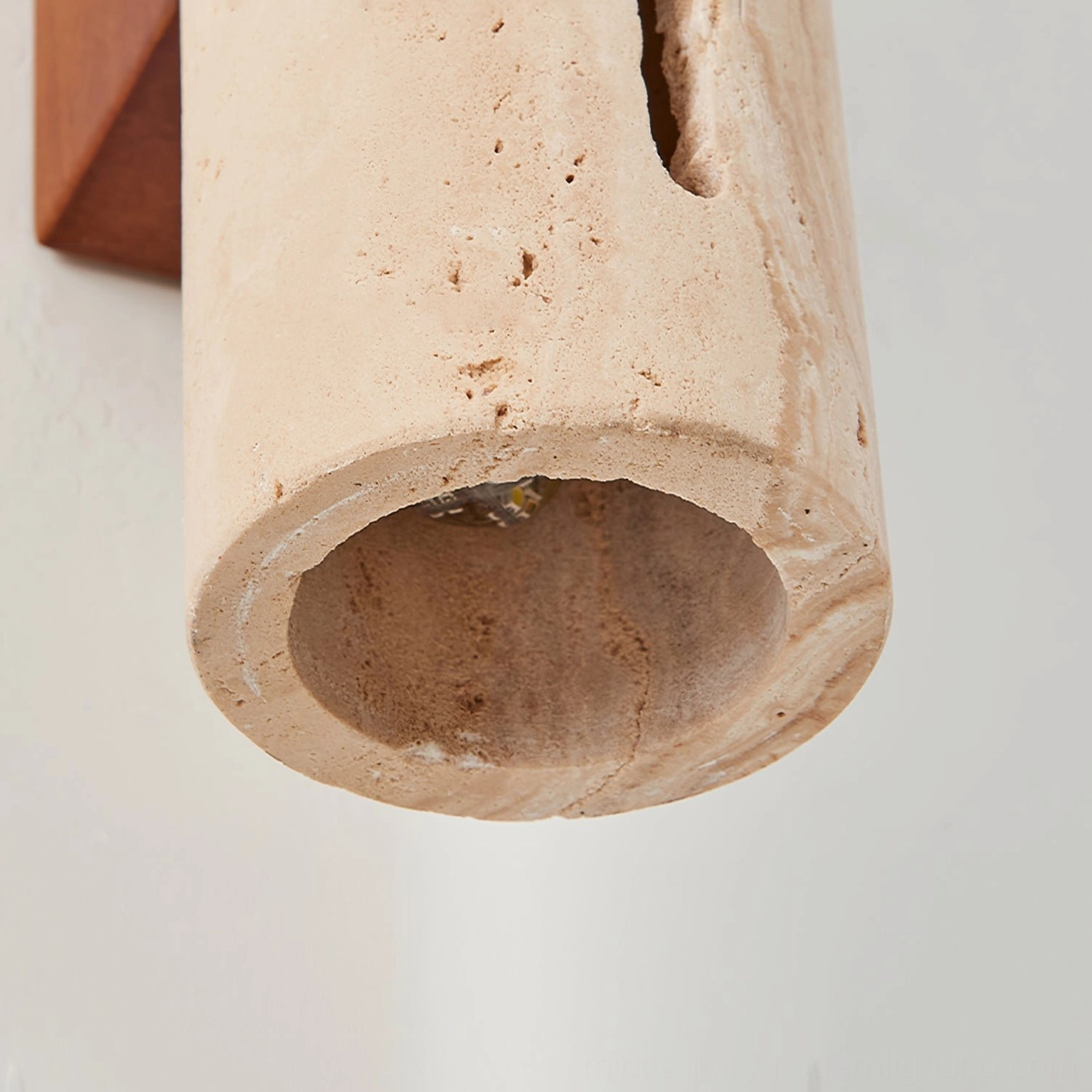 Bottom view of Lorelei travertine wall sconce showing hollow cylindrical stone body and rough texture with partial wooden mount