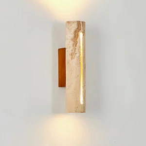 Lorelei travertine wall sconce lit on white interior wall, demonstrating warm ambient glow and natural stone veining pattern
