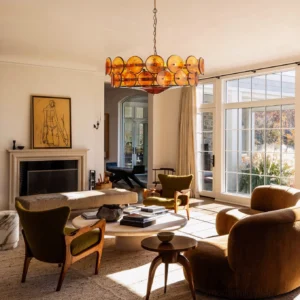 Amber orange Lorenzo chandelier installed in vintage living room with fireplace and warm earth-tone decor