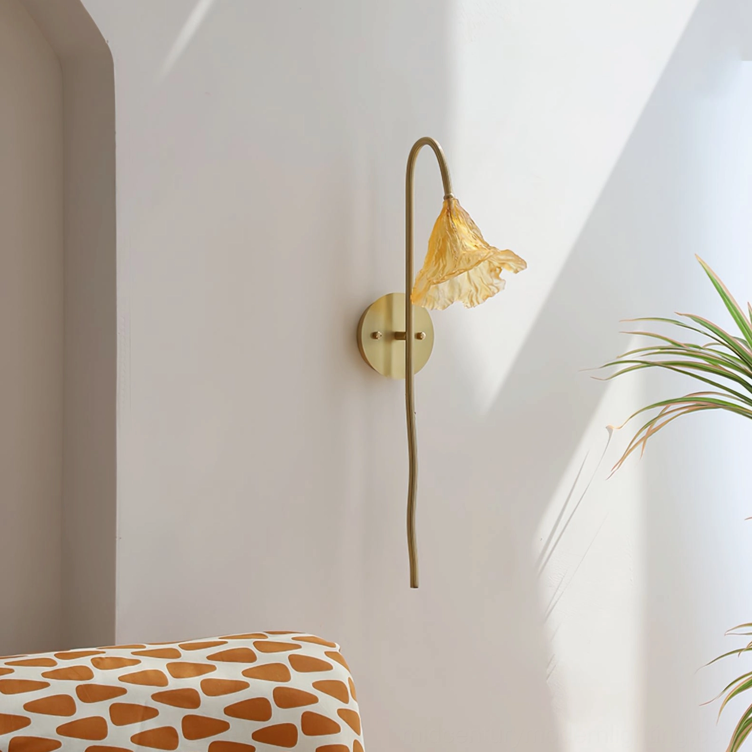 Lotus Amber Wall Sconce installed in bedroom corner with patterned upholstered furniture, showing curved lamp arm and brass base