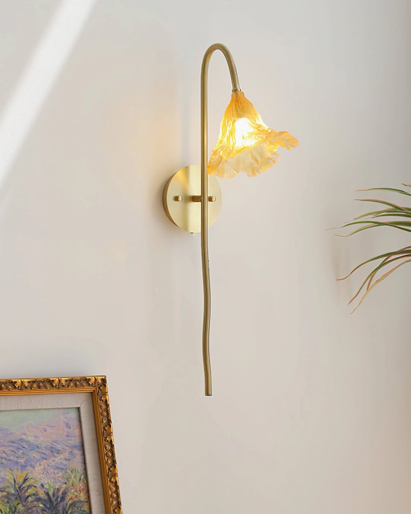 Lotus Amber Wall Sconce low side view with lit warm amber glass shade creating ambient lighting, curved lamp arm with framed artwork