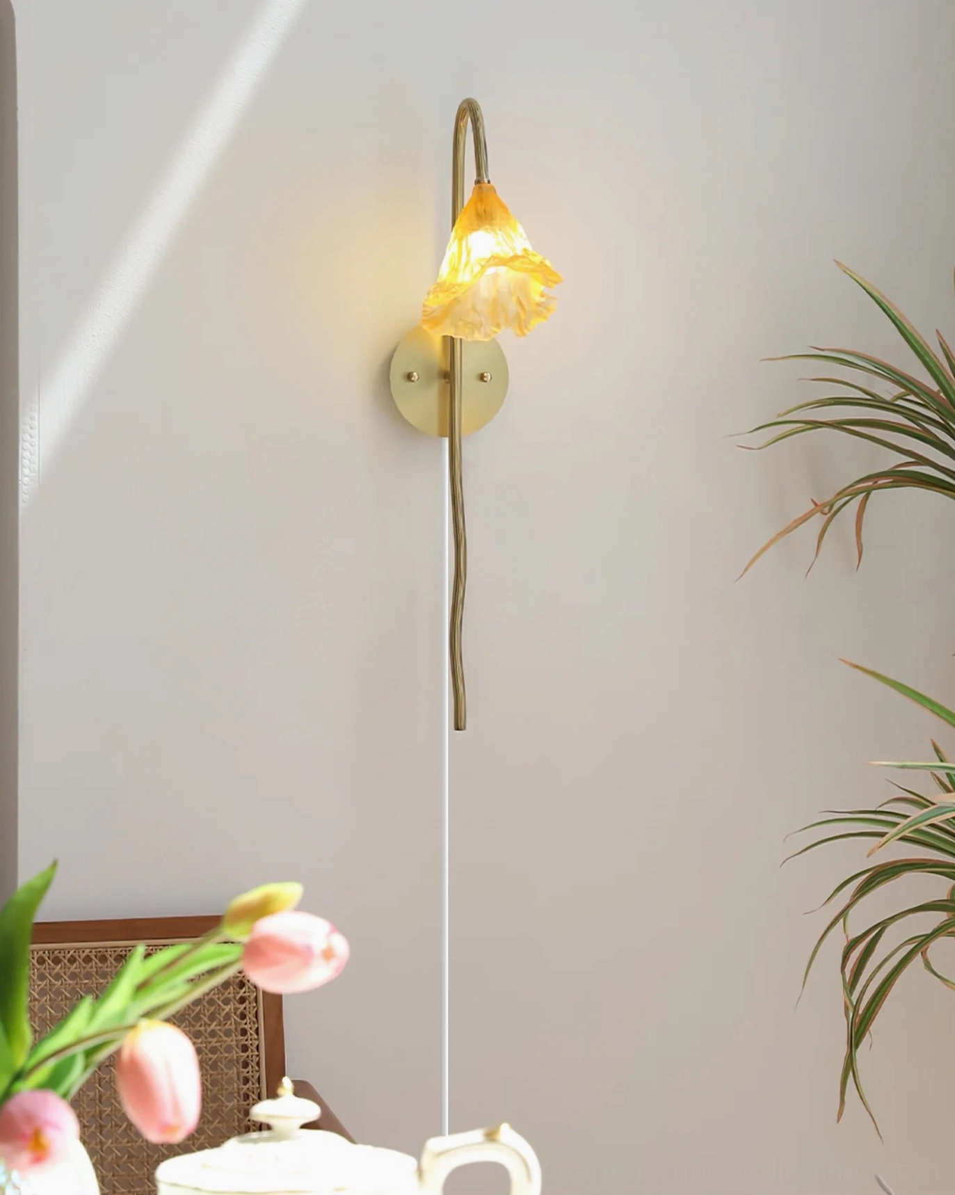 Lotus amber wall sconce lit with warm ambient light displayed on tabletop with tea set and fresh tulips