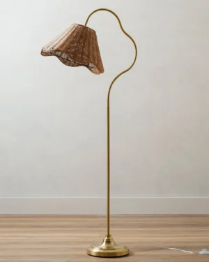 Lucinda mid-century modern rattan floor lamp in living room with wooden floor, three-quarter view showing brass curved arm