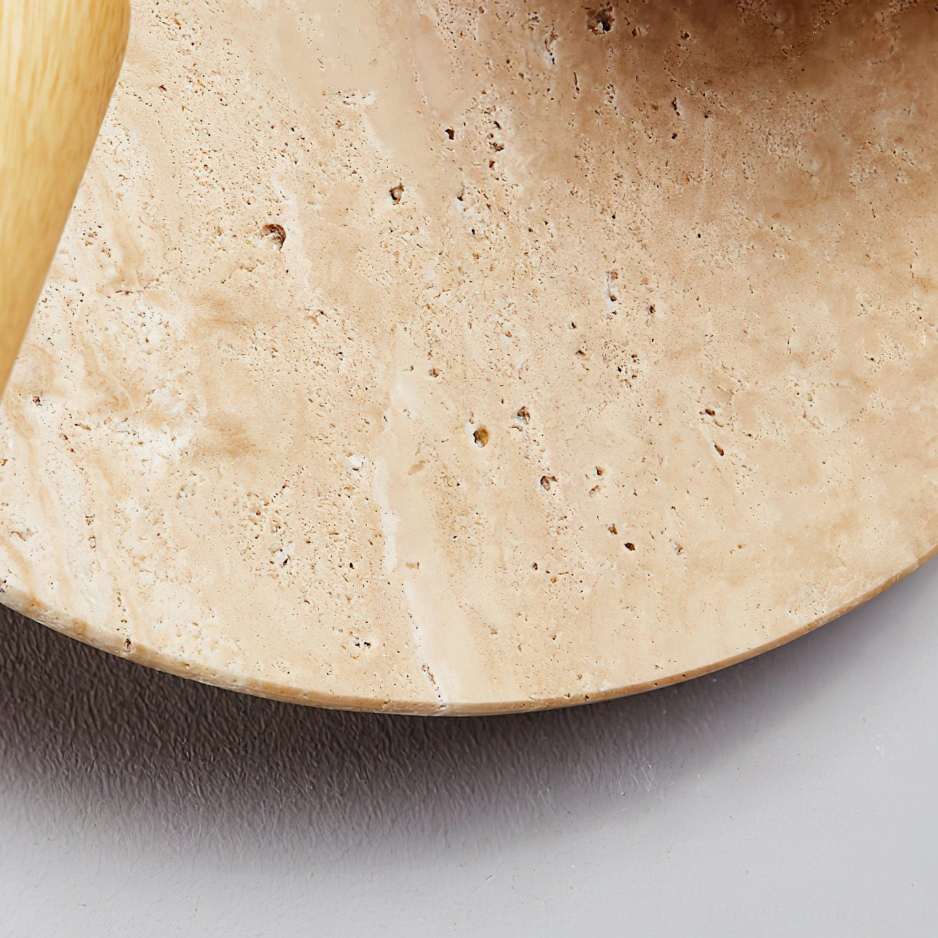 Close-up macro photograph of natural travertine stone texture showing porous surface and warm beige tones of Luka lamp backplate