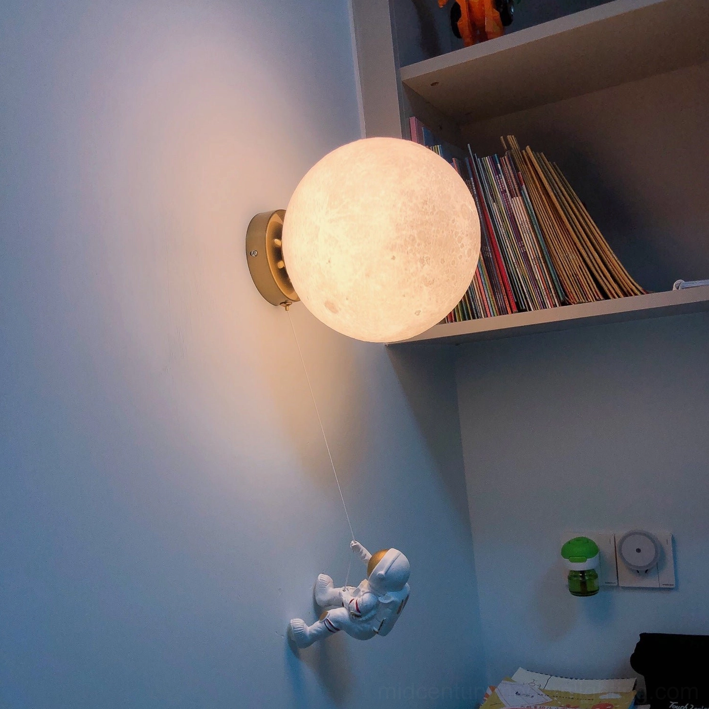 Lunar wall lamp with warm yellow lighting and silver-gold astronaut in home study with bookshelf