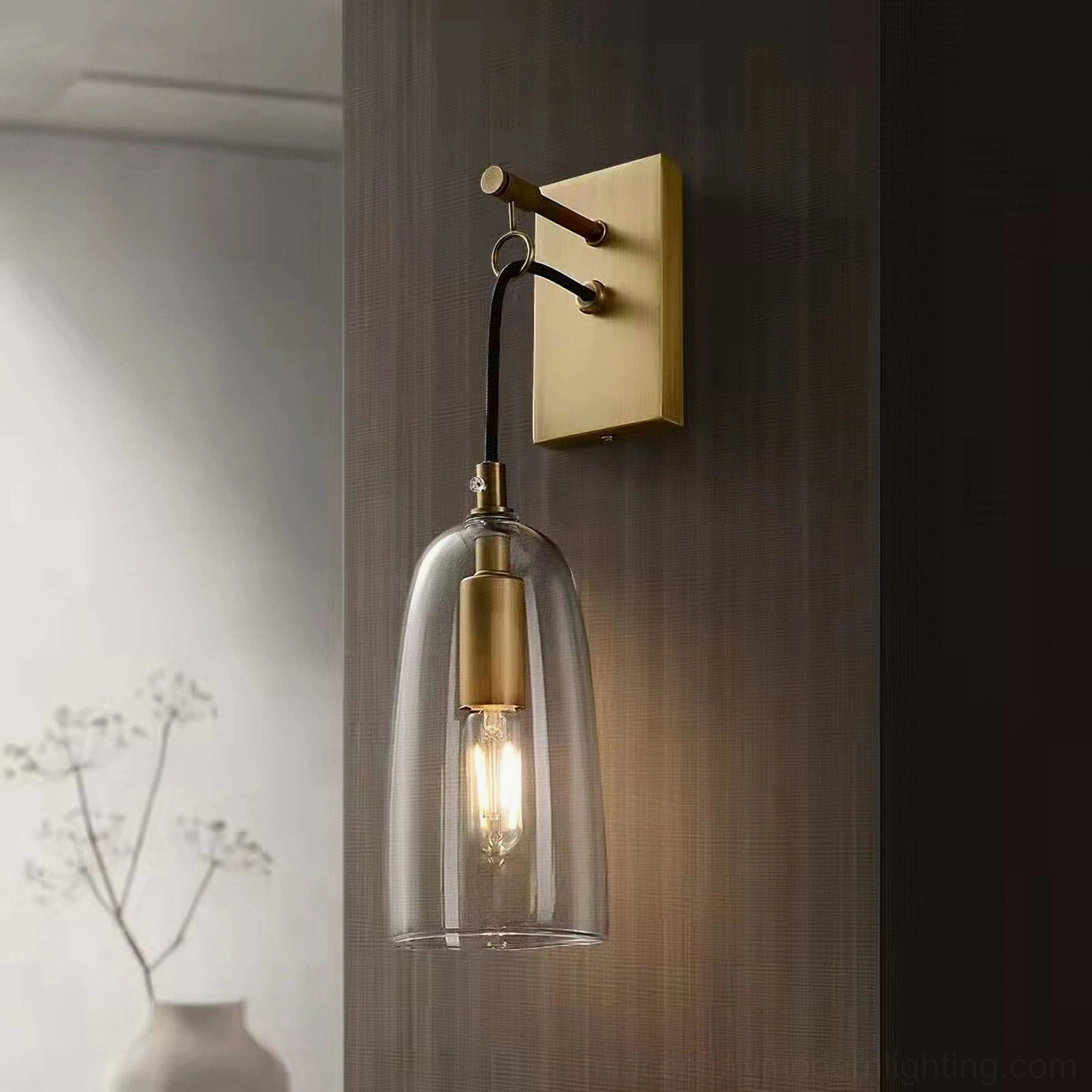 Brushed brass wall sconce casting warm ambient light, styled with dried flowers and wooden wall backdrop