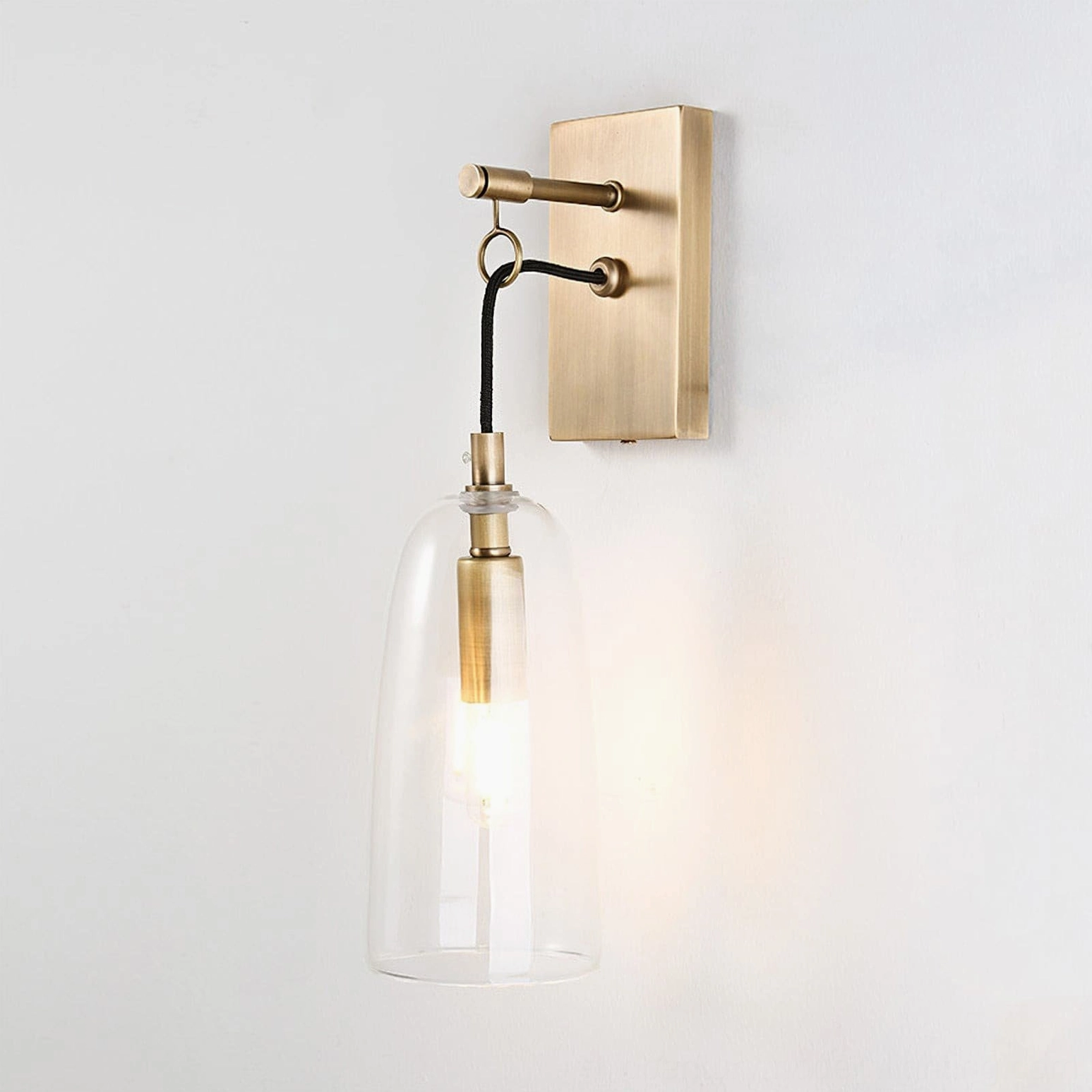 Polished brass wall sconce with illuminated Edison-style filament bulb, side-frontal view