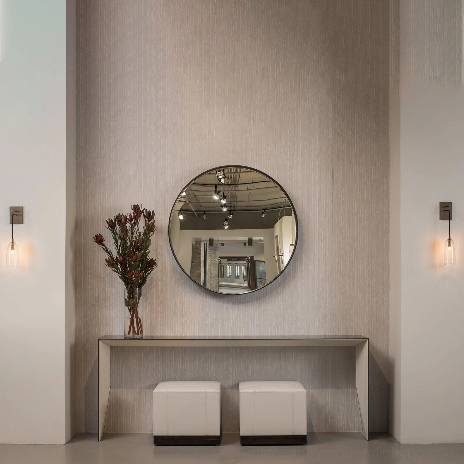 Pair of matching brass wall sconces flanking round mirror in modern entryway foyer